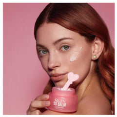Skin balm jar, pink container with white text, held by woman with product on face