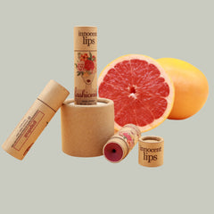 Lip balm tubes in brown cardboard with floral design and "Fashionista" text, next to grapefruit halves