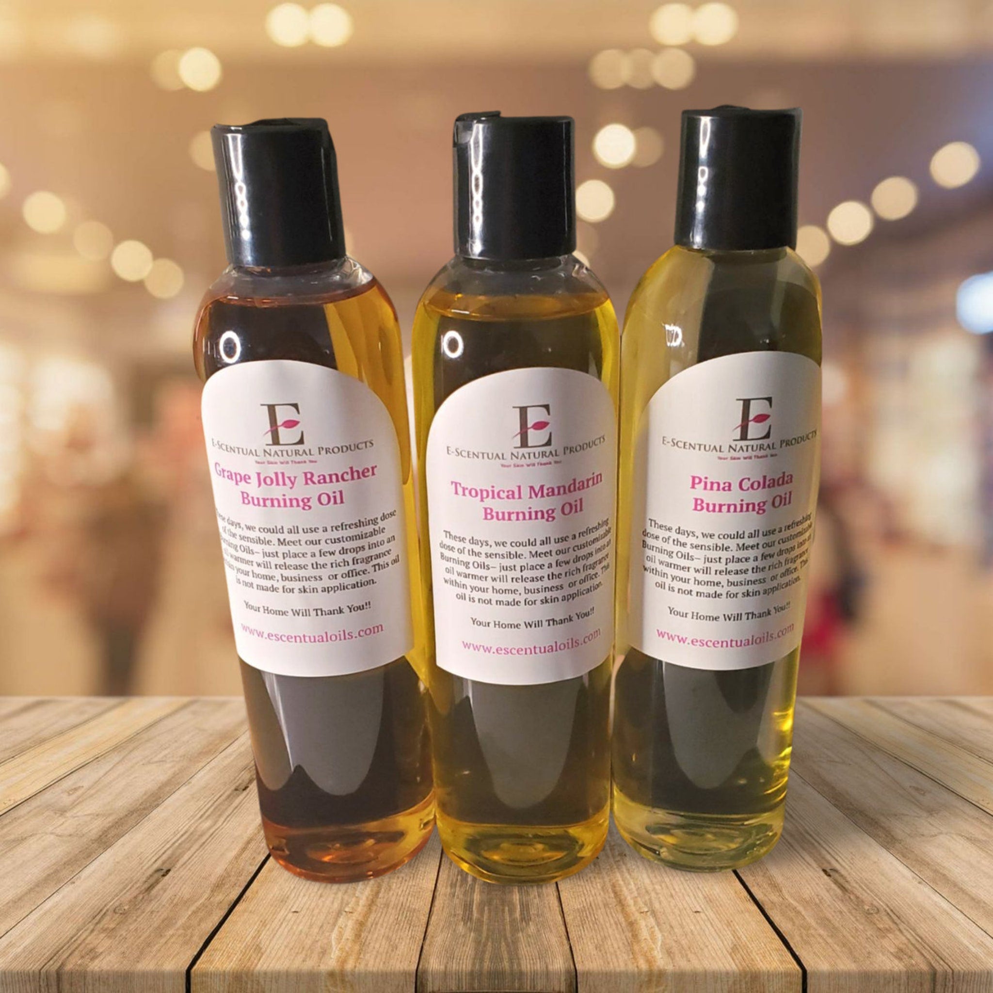 Burning oils in clear glass bottles with black caps, E-Scentual Oils brand, on wood surface.