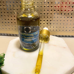 Nourishing Oil Cleanser bottle with gold cap and dropper, on a white marble surface, product label visible
