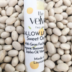 Lip balm tube with white label, orange accents, and "the Velvet" text, surrounded by white beans