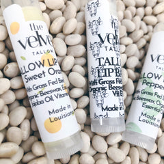 Lip balm tubes with white labels, black text, and cow illustrations on white beans background
