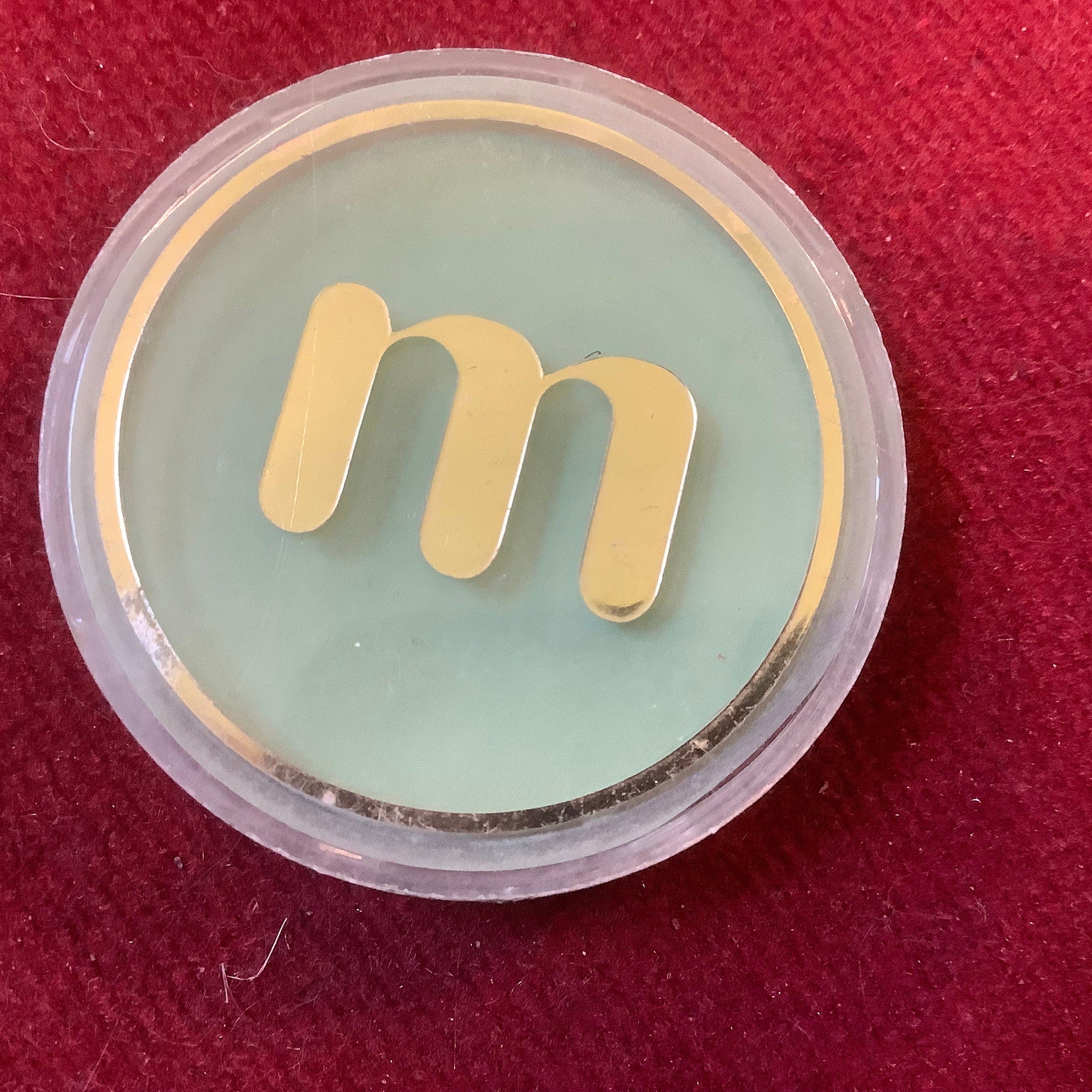 Eye makeup powder compact with gold "m" logo on green and clear plastic casing
