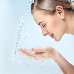 Woman's face with light skin tone, wet hair, and clear water splashing over her hands