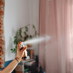 Spray bottle with brown glass, silver top, and white mist being sprayed