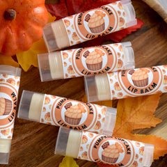 Lip balm tubes with orange and white labels, pumpkin cupcake design, on wooden surface