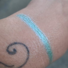 Close-up of duochrome eyeshadow pot showing vibrant color shift from teal to purple shimmer