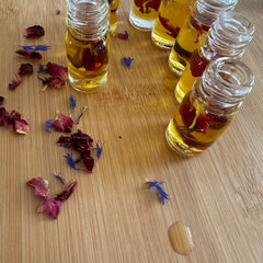 Small glass bottles with yellow liquid, red petals, and blue flowers on wood surface