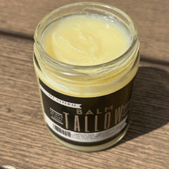 Tallow balm jar with pale yellow color, glass container, and black label with text on wood surface