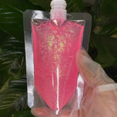 Wholesale lip gloss pouch with pink glitter base in clear plastic packaging held by gloved hand
