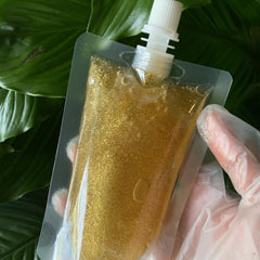 Lip gloss base gold glitter in clear pouch held by gloved hand