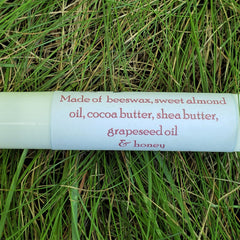 Lip balm tube with white and pink text on a green background of grass