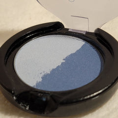 Eyeshadow compact with blue and white powder, black plastic case, and open lid