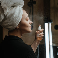 Facial mist bottle spraying, clear bottle, orange liquid, woman with towel on head