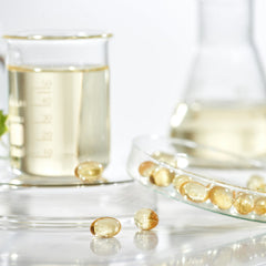 Capsule supplements, clear yellow softgels, glass dish, and beaker with liquid, health and wellness concept