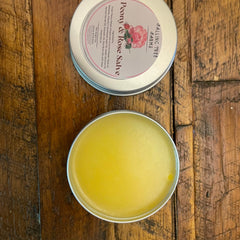 Peony & Rose Salve in metal tin with yellow salve and Falling Tree Farms label on wood surface