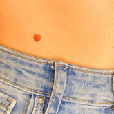 Body jewelry peach tattoo, small orange fruit design on skin, worn with denim jeans