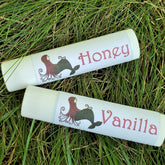 Lip balms, white tubes with red "Honey" and "Vanilla" text, Meadow Mermaids brand, on grass