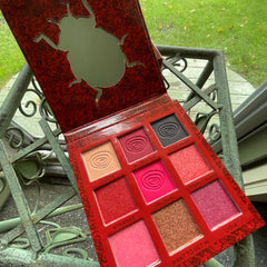 Eyeshadow palette with red case, patterned lid, and assorted color eyeshadows