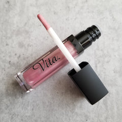 Lip gloss with pink color, clear tube, black cap, and "Vita" brand text visible