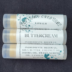 Lip balm tubes with white labels, teal splatter design, and Copeland Creations text visible on a dark surface.