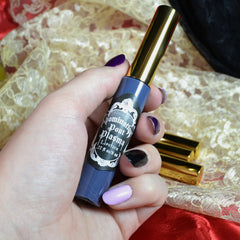 Lipstick tube in blue and gold with "Dominatrix Pout Plasma" label, held in hand with painted nails