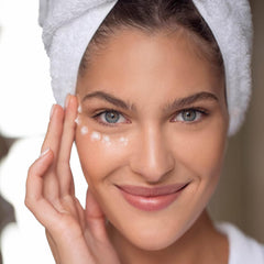 Eye cream application, woman with white towel, applying white cream to face, smiling