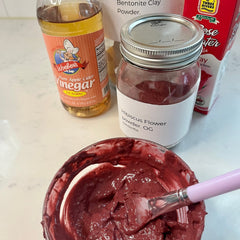 Face mask ingredients including red paste, clear glass jar, and Woebers apple cider vinegar bottle