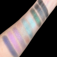Eyeshadow swatches with iridescent shimmer in various colors on skin, angled view, black background