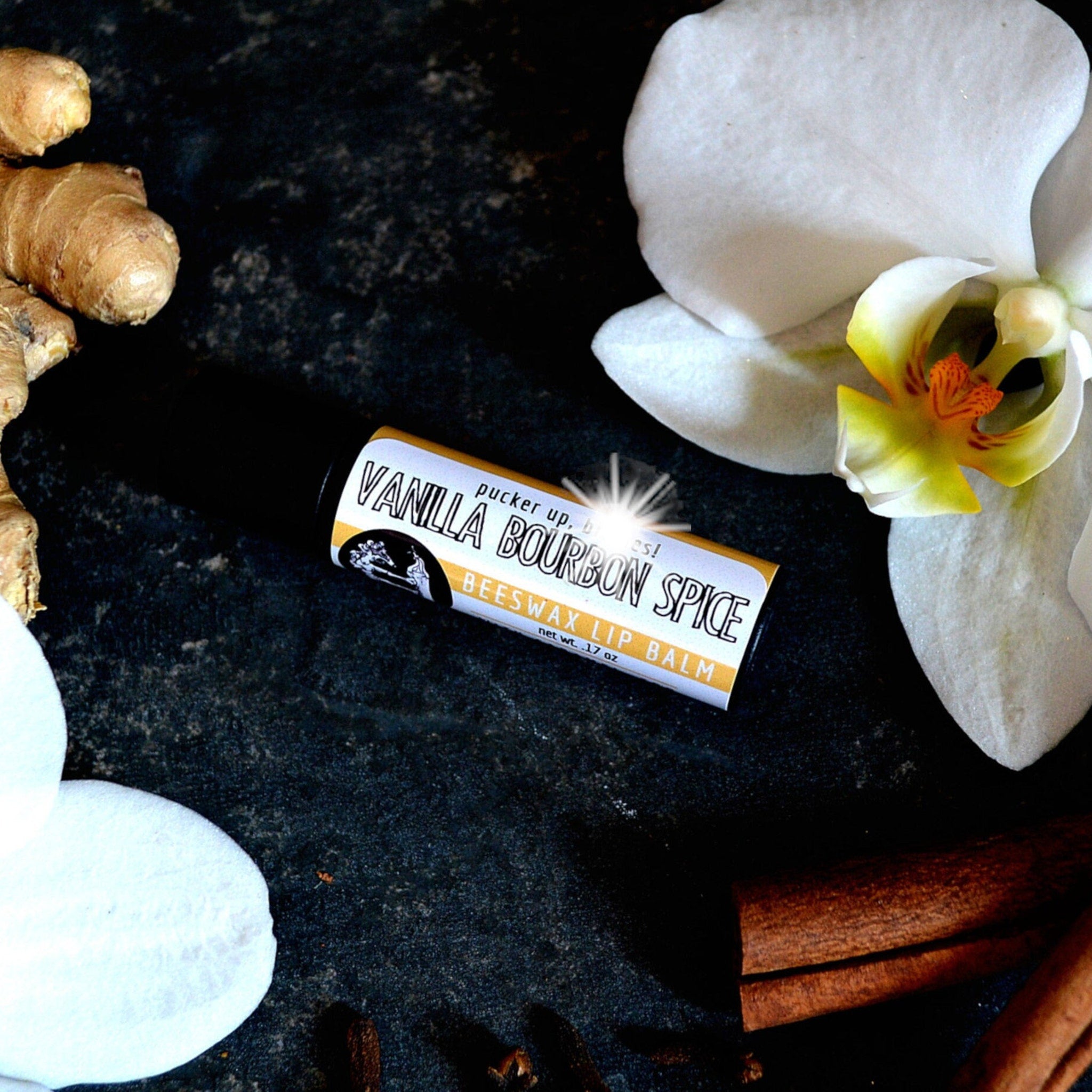 Lip balm tube with black and yellow label, white text, and floral arrangement