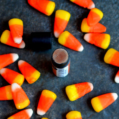 Candy corn with yellow, orange, and white layers scattered around a dark container of product