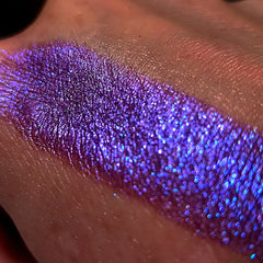 Purple eyeshadow swatch with glitter, iridescent shimmer, and skin background