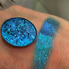 Eyeshadow compact with blue-green iridescent shimmer, shown swatched on skin