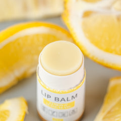 Lip balm tube with white and yellow packaging, pale yellow balm visible, with lemon slices in background