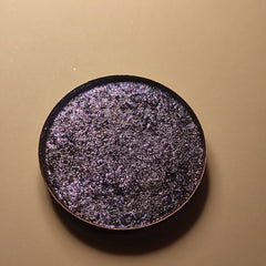 Eyeshadow compact with dark purple glitter and black rim on tan background