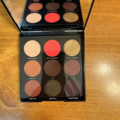 Eyeshadow palette with multiple colors including red, gold, and brown in a black compact.
