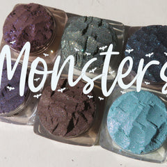 Six vibrant loose powder eyeshadows in shimmering shades displayed in round jars with black lids