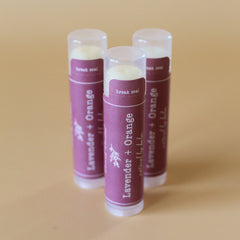 Lip balm tubes with purple label, clear cap, and white text, "Lavender + Orange