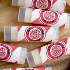 Candy Cane lip balm tubes with red and white striped design and clear plastic caps on wooden surface