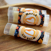 Lip balm tubes with maple label, clear plastic, and autumn leaf pattern on wood surface