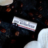 Lip balm tube with white and red label, surrounded by coffee beans and white shapes, BADGERFACE BEAUTY SUPPLY