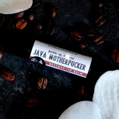 Lip balm tube with white and red label, surrounded by coffee beans and white shapes, BADGERFACE BEAUTY SUPPLY