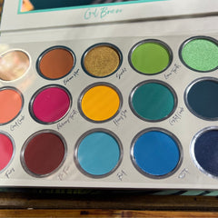 Eyeshadow palette with various colors, including green, blue, and gold, in a white case labeled Cool Breeze
