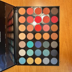 Eyeshadow palette with multiple colors in a black case, various shades of orange and blue.