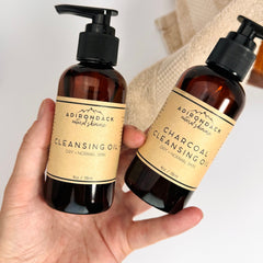 Cleansing oil bottles with brown glass, black pump tops, and tan labels, held by hand, Adirondack brand visible