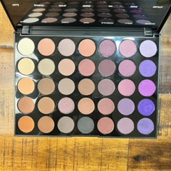 Eyeshadow palette with multiple colors in round pans, black case, and mirror lid.