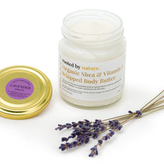 Hand scooping whipped shea butter from a glass jar, showing its rich creamy texture against moisturized skin