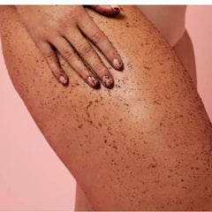 Body scrub on skin with brown speckled texture and hand with product on nails