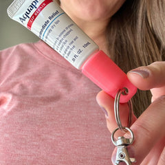 Lip balm keychain with pink cap and silver keyring, holding Aquaphor tube