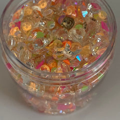 Decorative craft beads in clear, orange, pink, and green colors, inside a clear container